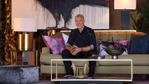 Steven Sabados sitting on a sofa with products from his Mystere Studio Collection