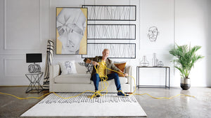 Steven Sabados sitting on a sofa while stretching a yellow cord surrounded by products from his Wired Studio collection 